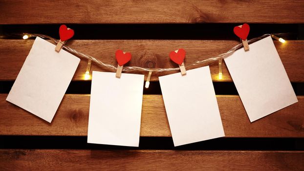 Blank White Piece of Paper hanging on Light Garland with Decorative Love Pins. Valentines Day Background with Copy Space. Cozy Wooden Background