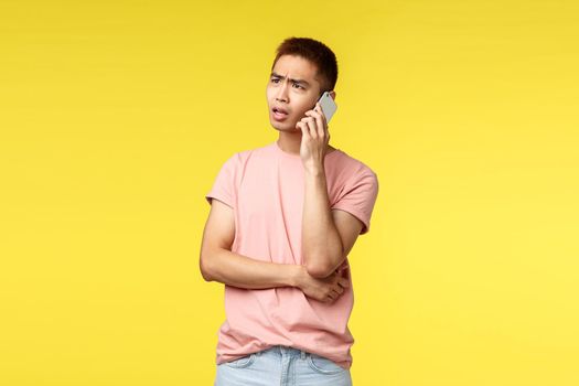 Technology, communication and lifestyle concept. Portrait of frustrated, disappointed asian guy talking on phone, discuss problem on phone, use smartphone and frowning complicated.