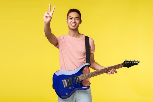 Lifestyle, leisure and youth concept. Peace my friends. Portrait of enthusiastic handsome asian guy playing on stage, performing song, holding electric guitar, invite listen to his band.