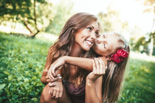 Beautiful mother and daughter having fun at the park in spring day hugging and kissing.