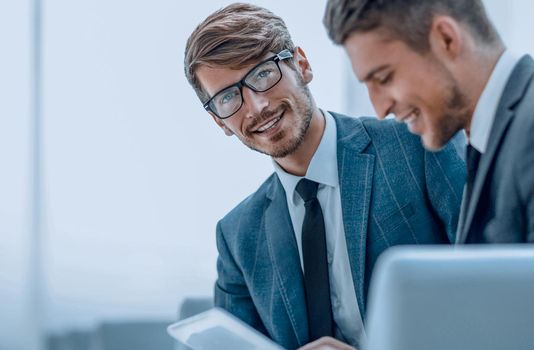 Smiling young businessman discussing something positive with his colleague, and using a digital tablet together