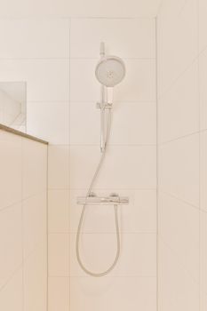 Shower faucets attached to tiled wall near glass partition and ornamental curtail in washroom at home