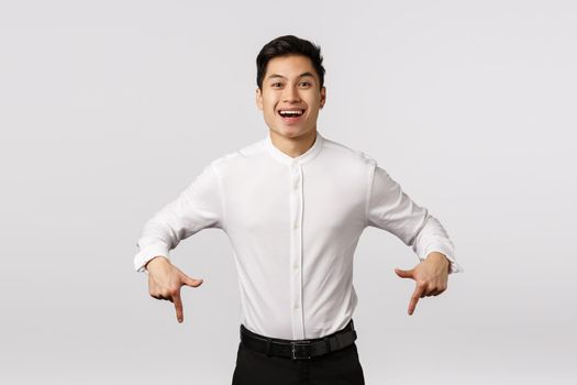 Happy and pleased successful asian male student, entrepreneur winning and asking check out something, smiling proud and delighted, looking camera, promoting cool product, white background.