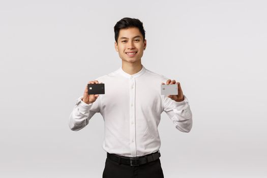 No cash needed with this bank. Pleased and sassy handsome asian young male entrepreneur, holding two credit cards black and white platinum, smiling satisfied, recommend payment method.