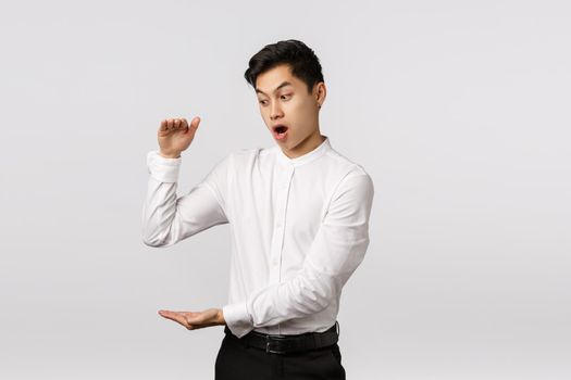 Omg businessman shocked how fast finances increase. Astonished and impressed, excited asian male employee getting rich fast, showing something big, shaping large box, white background.