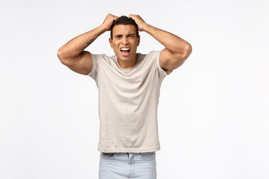 Disappointed athletic man in t-shirt, grab head and pull hair bothered, frowning grimacing shocked and frustrated, lost huge money, feel betrayed or let down, standing distressed white background.