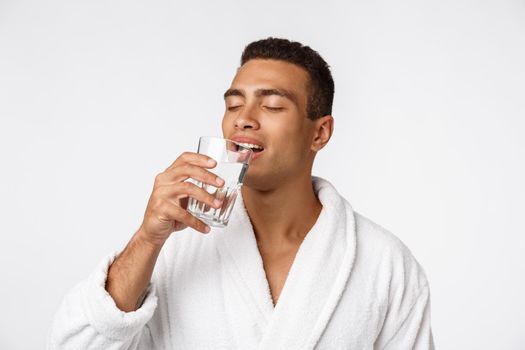 An attractive man drinking a glass of water against white background.