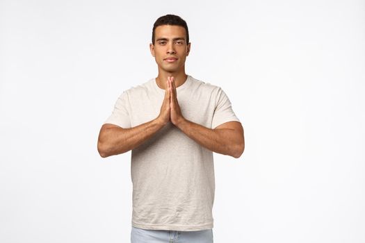 Peaceful good-looking strong, athletic young man in casual t-shirt, press hands together over chest in namaste, nirvana pose, look patient and calm, release stress in meditation, practice yoga.