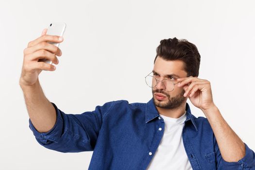 Portrait of an attractive young man taking a selfie while standing and pointing finger isolated over white background