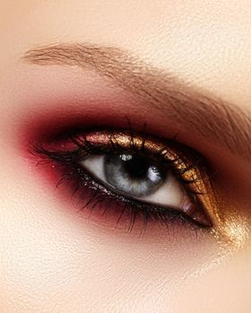 Closeup female eye with fashion bright make-up. Beautiful gold, red eyeshadow, wet glitter, black eyeliner. Perfect Shape of Eyebrows