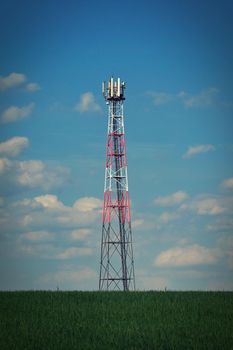 Transmitter for gsm signal of mobile phones in the field. In the background blue sky with clouds. Concept for modern technology and industry - Telecommunication Tower.