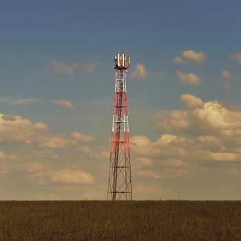 Transmitter for gsm signal of mobile phones in the field. In the background blue sky with clouds. Concept for modern technology and industry - Telecommunication Tower.