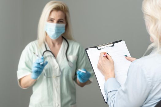 Middle aged female doctor therapist in medical mask on consultation with patient in office.