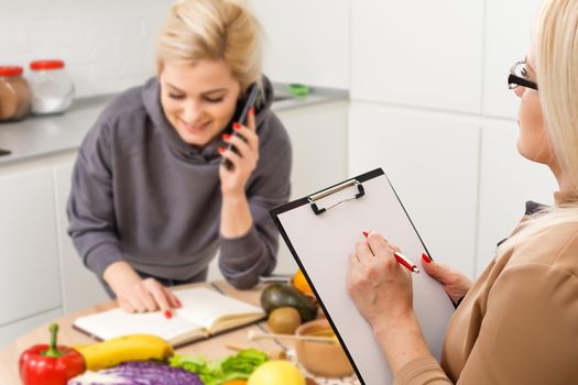 A smiling nutritionist advises a young patient woman on proper nutrition and dieting. The doctor shows a scheme of weight loss without a bad effect on health.