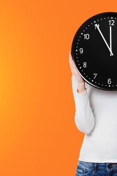 Woman with clock over face on bright orange background. Time concept