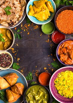 Assorted indian food on dark wooden background. Dishes of indian cuisine. Curry, butter chicken, rice, lentils, paneer, samosa, naan, chutney, spices. Space for text. Bowls and plates with indian food