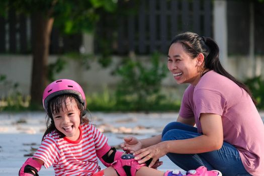 Asian mother helps daughter practice roller skating in the park. Exciting outdoor activities for kids.