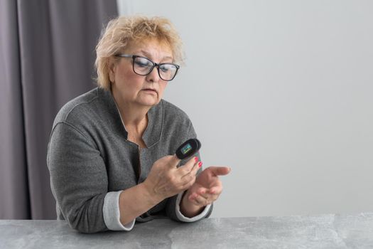 Hand of senior woman with an attached pulse oximeter on fingertip,old elderly measuring heart rate, checking oxygen saturation level in the blood, diagnosis of Coronavirus, COVID-19 at home, health care.