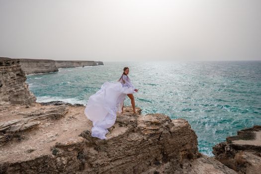 Happy freedom woman on the beach enjoying and posing in white dress over the sea. View of a girl in a fluttering white dress in the wind. Holidays, holidays at sea