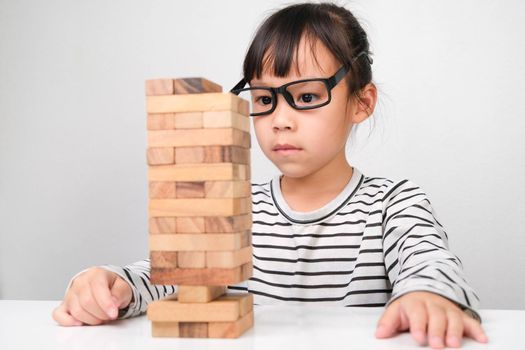 Asian children playing wooden blocks on table at home. Cute little girl having fun playing with building blocks. Wooden block tower building game. Toys for the development of children