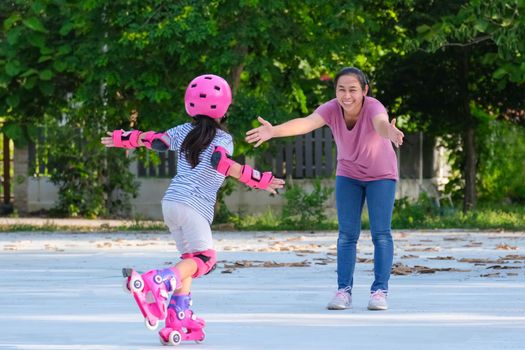 Asian mother helps daughter practice roller skating in the park. Exciting outdoor activities for kids.