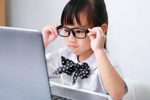 Cute Asian little girl playing teacher role game or a small businesswoman working with laptop in the office. Homeschool children's play and learning.
