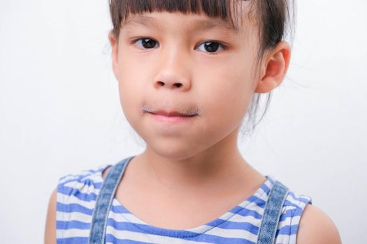 Cute little girl holding a glass of milk and licking her lips on white background. Small girl at home with smiling face, feeling happy enjoying drinking milk and looking at camera.