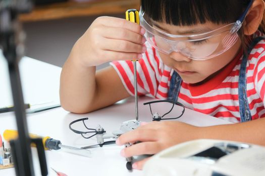 Concentrated little girl repairing her toy drone with a tool in hand and carefully assembles toy drone with screwdriver. STEM Hobbies for advanced smart kids.