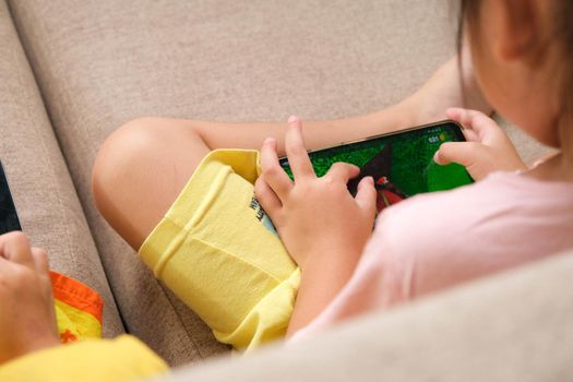 Two little girls addicted to mobile phones. Asian sisters are playing games or watching cartoons with their smartphones on the sofa at home.