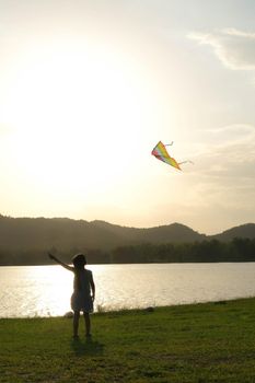 Child playing with a kite while running on a meadow by the lake at sunset. Healthy summer activity for children. Funny time with family.