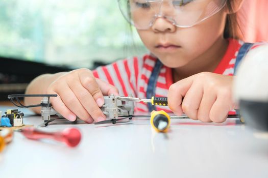 Concentrated little girl repairing her toy drone with a tool in hand and carefully assembles toy drone with screwdriver. STEM Hobbies for advanced smart kids.