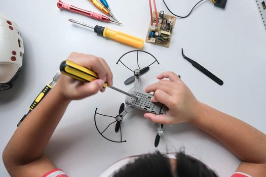 Concentrated little girl repairing her toy drone with a tool in hand and carefully assembles toy drone with screwdriver. STEM Hobbies for advanced smart kids.