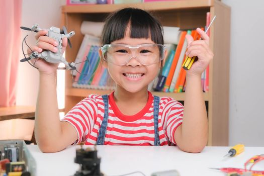 Concentrated little girl repairing her toy drone with a tool in hand and carefully assembles toy drone with screwdriver. STEM Hobbies for advanced smart kids.