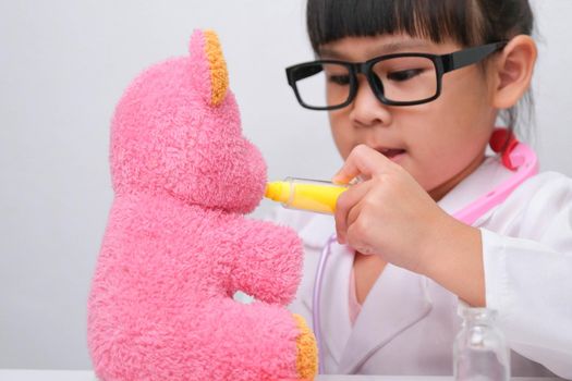 Cute Asian little girl playing doctor role game is giving injection to her sick teddy bear friend. Homeschool children's play and learning.
