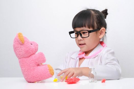 Cute Asian little girl playing doctor role game is giving injection to her sick teddy bear friend. Homeschool children's play and learning.