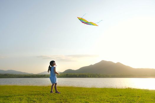 Child playing with a kite while running on a meadow by the lake at sunset. Healthy summer activity for children. Funny time with family.