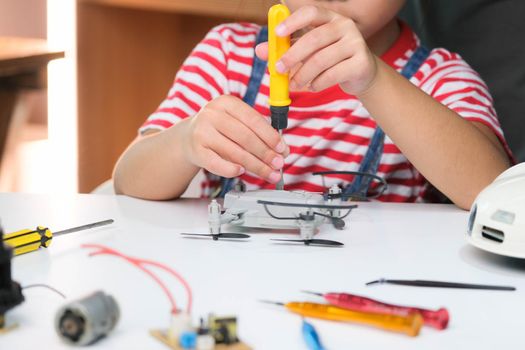 Concentrated little girl repairing her toy drone with a tool in hand and carefully assembles toy drone with screwdriver. STEM Hobbies for advanced smart kids.