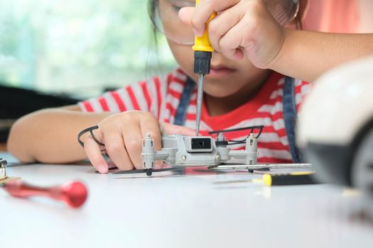 Concentrated little girl repairing her toy drone with a tool in hand and carefully assembles toy drone with screwdriver. STEM Hobbies for advanced smart kids.