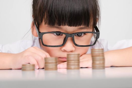 Cute asian little girl making stacks of coins. Little kids save money for future education.