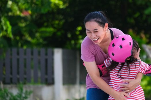 Asian mother helps daughter practice roller skating in the park. Exciting outdoor activities for kids.