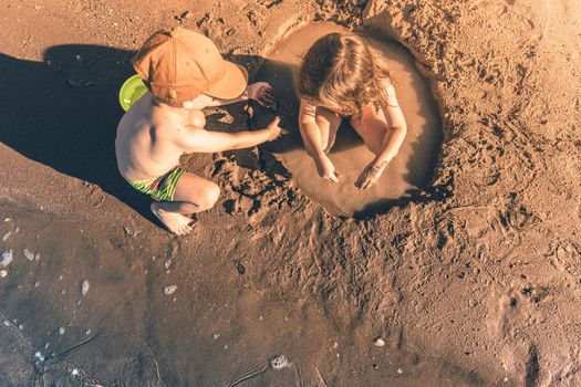 Boy and girl playing with sand by the sea. Top view, copy space.