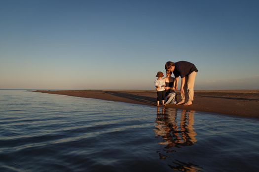 Young parents spend time with their child on the beach by the sea. Beautiful reflection in the water, copy space.