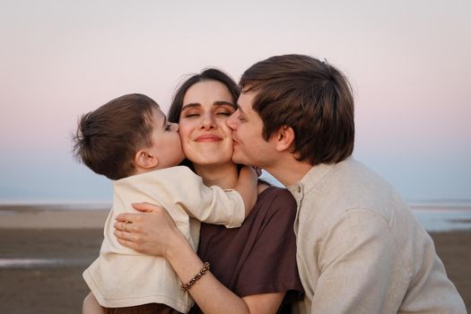 Young father with his little son kissing his wife and mother. Family look linen clothes.