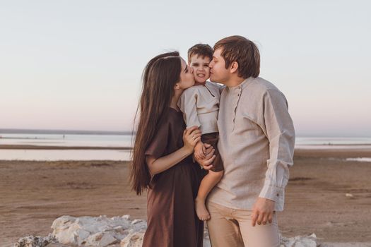 Family look of natural linen clothing on the evening beach. Young family hugs and kisses.