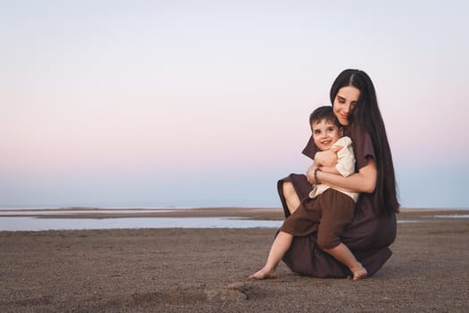 Happy mother and son having fun together. Mother gently hugs her little cute son outdoor. Family look linen clothes. Copy space.