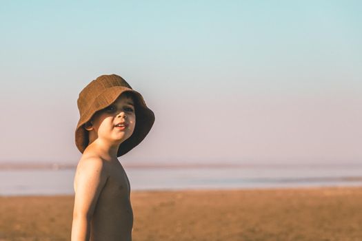 Portrait of a little boy 3 years old in a brown panama hat on the beach. Copy space