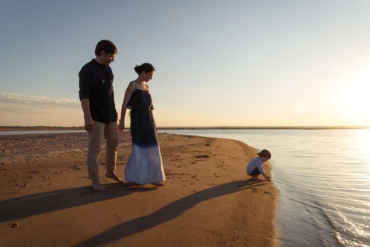 A young family with a 3 year old son is walking along the wild evening beach. Copy space.