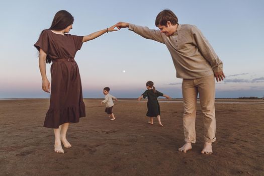 Young parents with two small children play and dance in the evening on the beach.