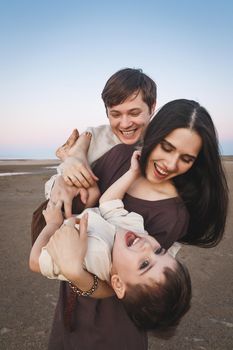 Happy laughing young family vertical portrait on the evening beach. Family look linen clothes.