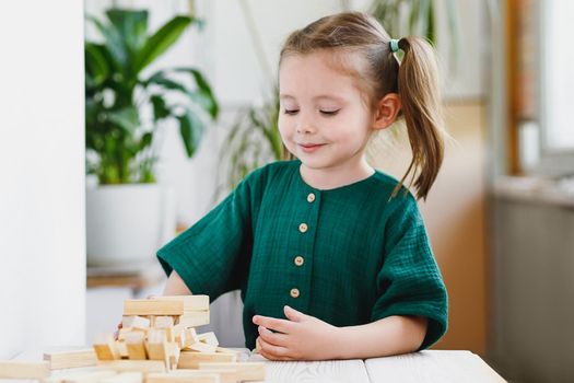 Beautiful cute preschool girl plays at home with wood blocks on table. Natural tactility development.